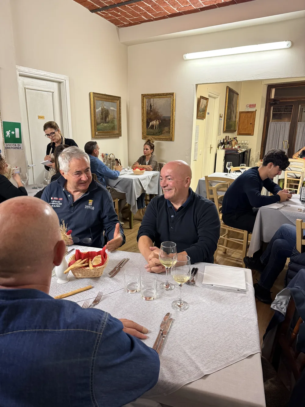 Clienti a tavola che chiacchierano sotto la volta in mattoni, con i quadri alle pareti.