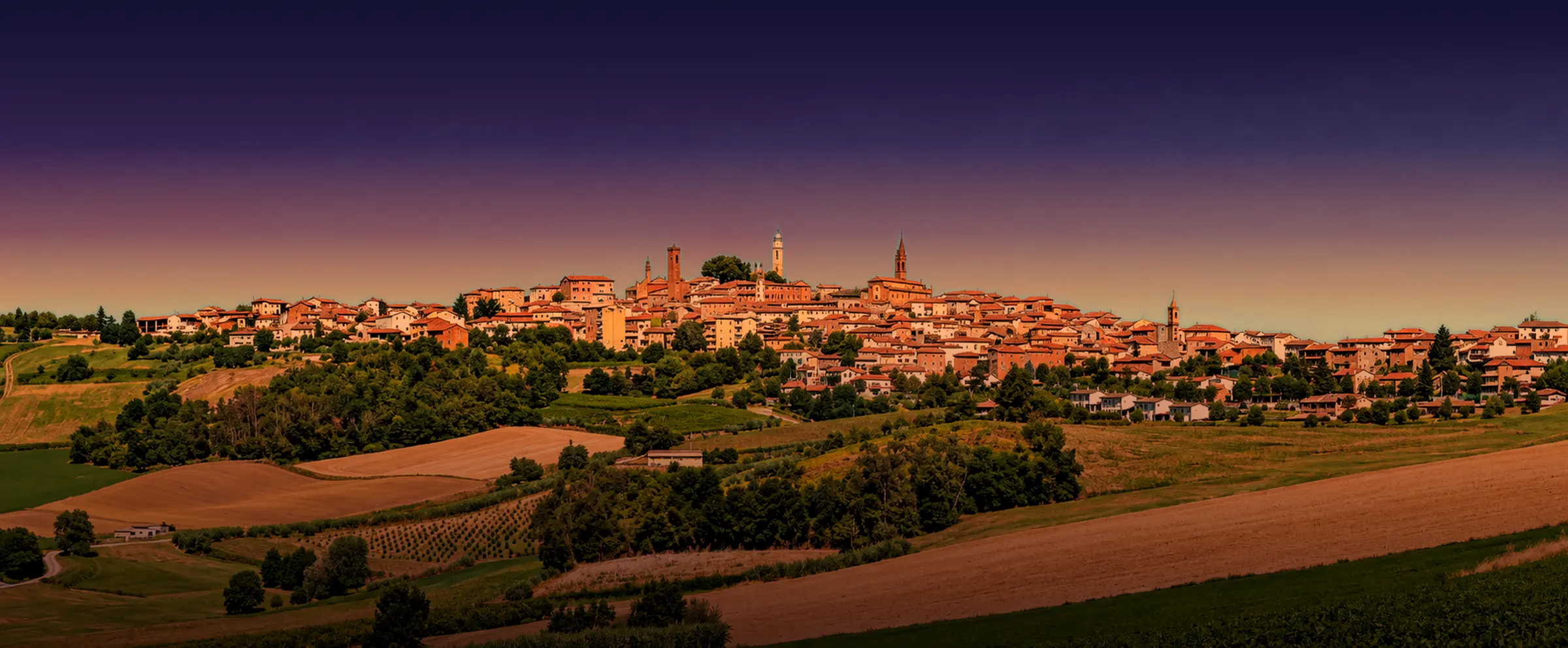 Lu, nel Monferrato, vista dalle colline all'ora del tramonto: il paese sul crinale con i suoi campanili, sopra campi e vigneti.
